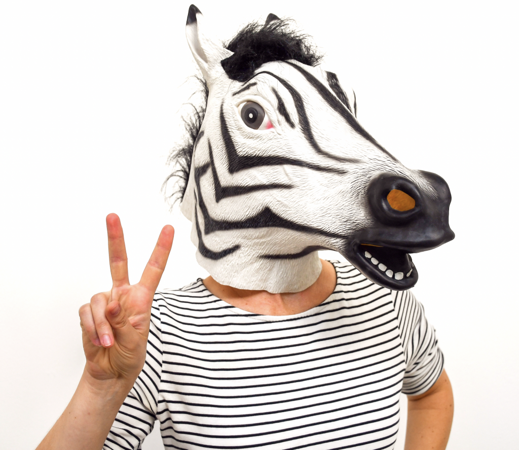 A person with a zebra mask, wearing a zebra-striped T-shirt, doing the peace sign